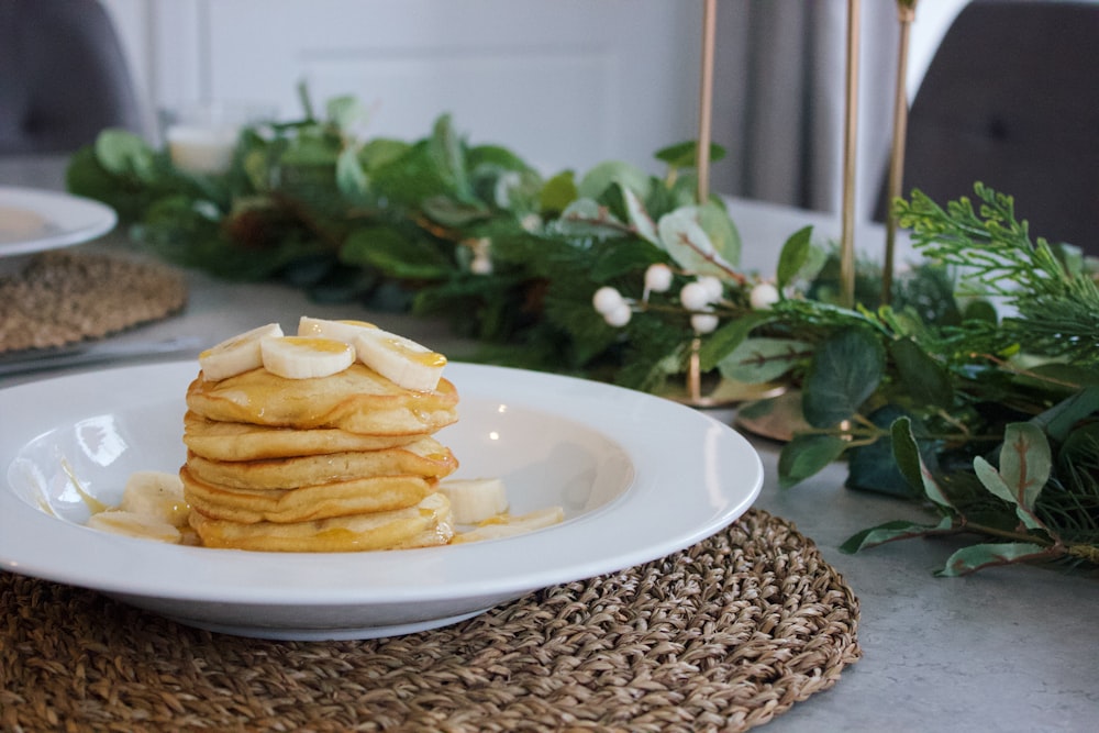 pile of pancakes on white plate near green leaves