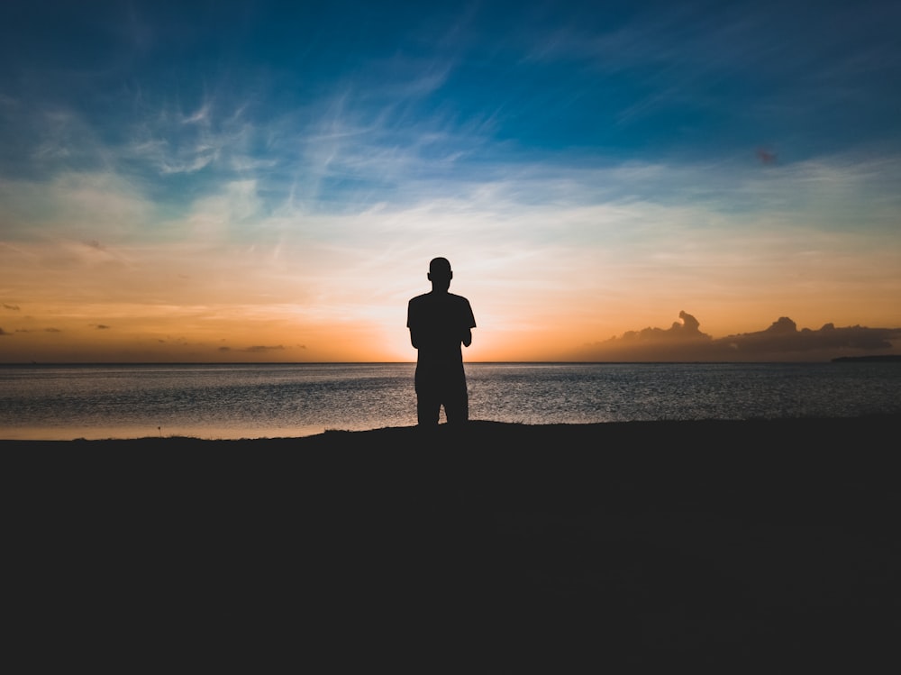 silhouette photo of man standing near seashore