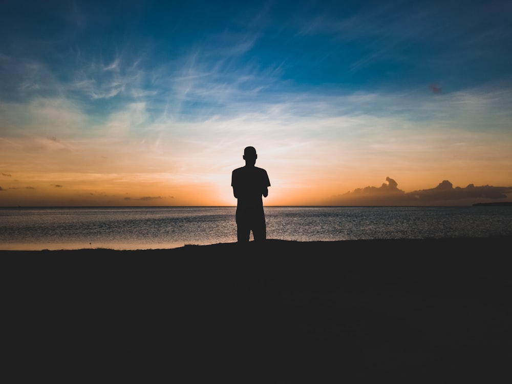 photo de silhouette d’homme debout près du bord de mer