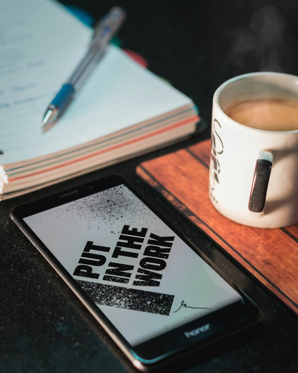 Honor smartphone beside mug and paper with pen