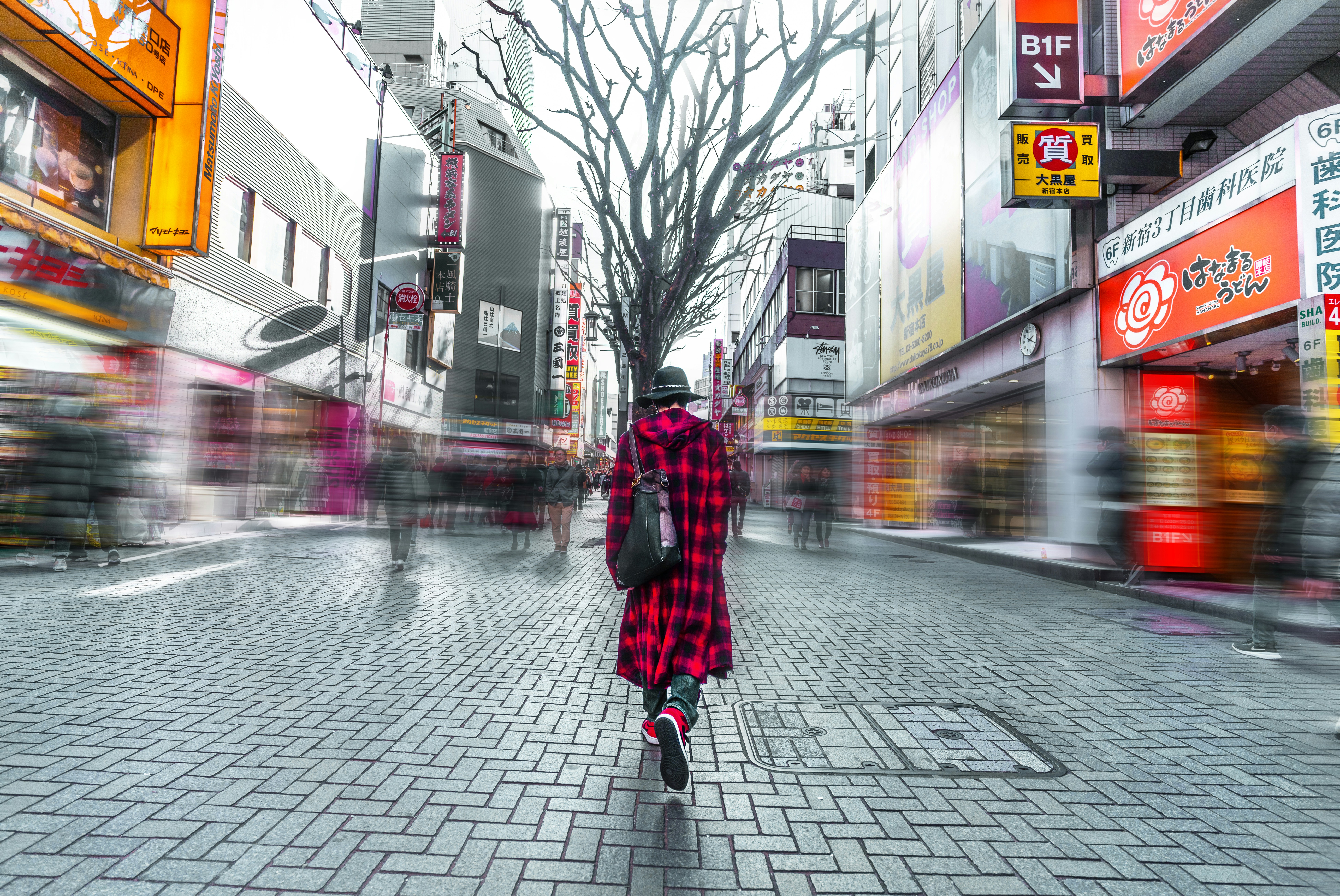 selective focus photography of person wearing hat, red-and-black check coat walking on busy street during daytime