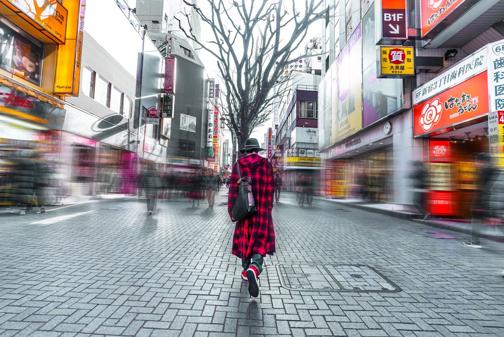 selective focus photography of person wearing hat, red-and-black check coat walking on busy street during daytime