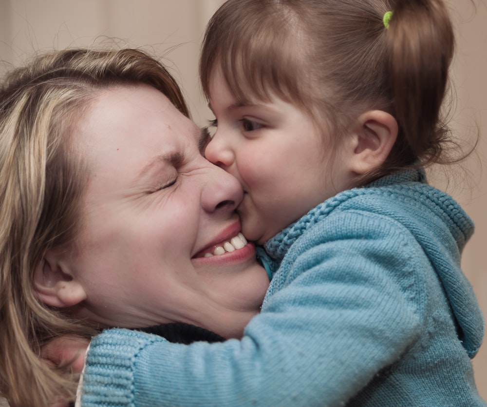 woman carrying girl while toddler kissing her nose