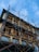 A multi-story building is under construction or renovation, surrounded by metal scaffolding. The structure features a series of wooden-framed windows and decorative railings. The sky above is mostly clear with patches of clouds.