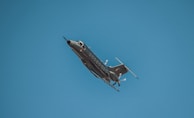 A sleek military aircraft is flying through a clear blue sky, showcasing its aerodynamic design and propellers.