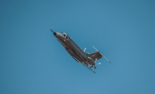 A sleek military aircraft is flying through a clear blue sky, showcasing its aerodynamic design and propellers.