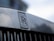 Close-up of a metallic surface with the Rolls-Royce emblem prominently displayed. The emblem consists of two overlapping 'R' letters with the words 'ROLLS' and 'ROYCE' above and below the letters. The background is softly blurred, giving a focus to the emblem.