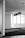 A modern office space featuring several large windows allowing ample natural light. The ceiling has a grid-like pattern with multiple hanging lights. The floor is carpeted and the walls are mostly blank, contributing to a minimalist aesthetic.