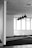 A modern office space featuring several large windows allowing ample natural light. The ceiling has a grid-like pattern with multiple hanging lights. The floor is carpeted and the walls are mostly blank, contributing to a minimalist aesthetic.