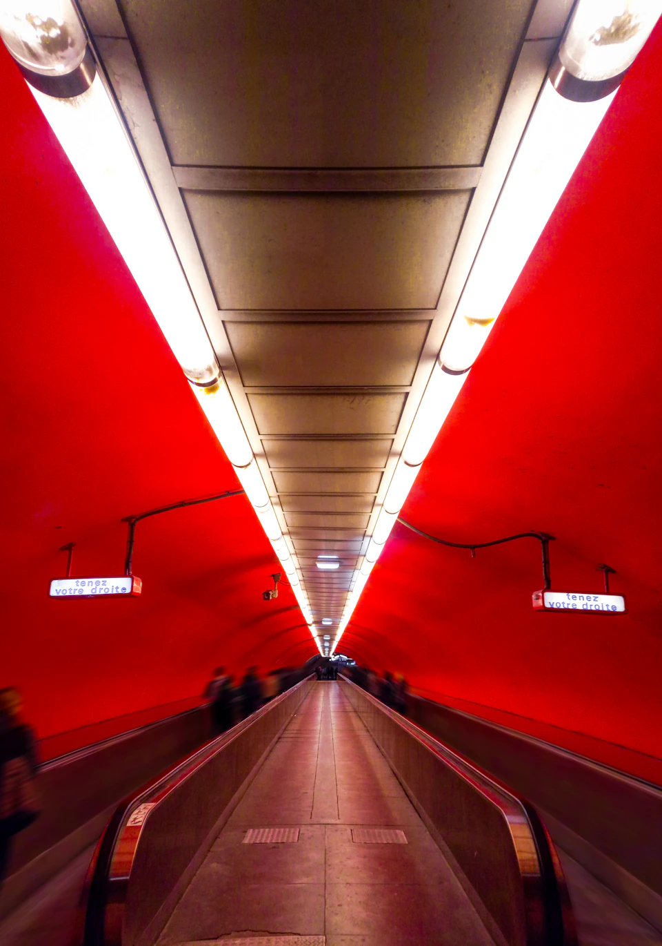 Long, narrow tunnel with red ceiling and glowing walls under soft white lighting