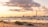 A coastal industrial landscape during sunset, featuring a sandy beach in the foreground with rocks scattered along the shore. In the distance, there are several industrial structures, including cranes and smokestacks silhouetted against the sky. The sky is filled with a mix of clouds, illuminated by the warm glow of the setting sun.