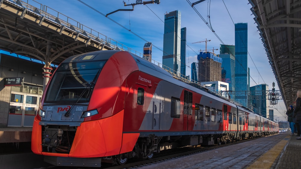 red and gray train beside concrete buildings