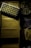 A tray of ammunition cartridges is placed on top of two boxes labeled 'Winchester, 50 Cartridges, Caliber 9mm, Full Metal Jacket, Service Grade.' Beside the boxes is a round plastic container filled with additional loose cartridges. The scene is dimly lit with a shadowy ambiance.