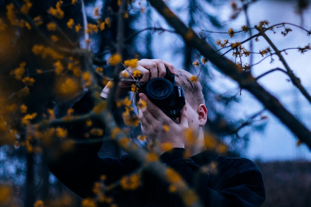 selective focus photography of man holding Canon DSLR camera