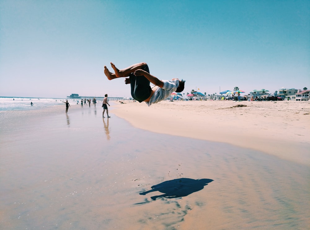 man back flipping in seashore during daytime