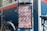 A signage indicating directions to Kyoto, Osaka, and Nara is mounted on a street pole. The sign has a striped red and white background with bold black letters. A bicycle is partially visible in the background, alongside a blue wall adorned with various stickers and logos. The sign also mentions 'Explorer Map' and 'Guide Map' with additional text in both English and Japanese.