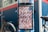 A signage indicating directions to Kyoto, Osaka, and Nara is mounted on a street pole. The sign has a striped red and white background with bold black letters. A bicycle is partially visible in the background, alongside a blue wall adorned with various stickers and logos. The sign also mentions 'Explorer Map' and 'Guide Map' with additional text in both English and Japanese.