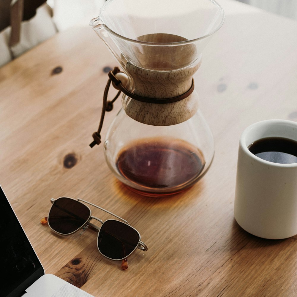 Sonnenbrille in der Nähe von Teekanne und gefüllter Tasse