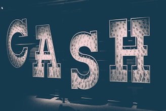 Large illuminated letters spell out the word 'CASH' against a dark background, with each letter filled with lightbulbs that produce a soft, glowing effect.