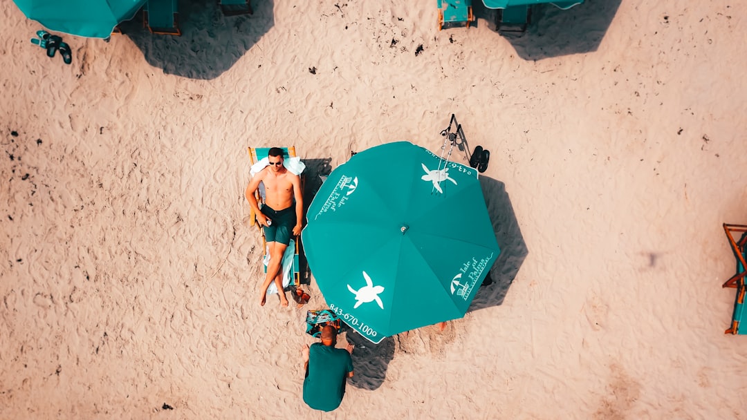 man lying on lounge under umbrella during daytime \