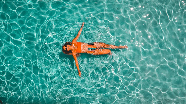 Seen from above, a swimmer floats on her back in clear turquoise water