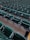 Rows of empty green stadium seats, each with integrated cup holders, are aligned in a uniform pattern. The seats are arranged in an orderly fashion on concrete flooring, suggesting a venue setup for sports or events.
