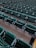 Rows of empty green stadium seats, each with integrated cup holders, are aligned in a uniform pattern. The seats are arranged in an orderly fashion on concrete flooring, suggesting a venue setup for sports or events.