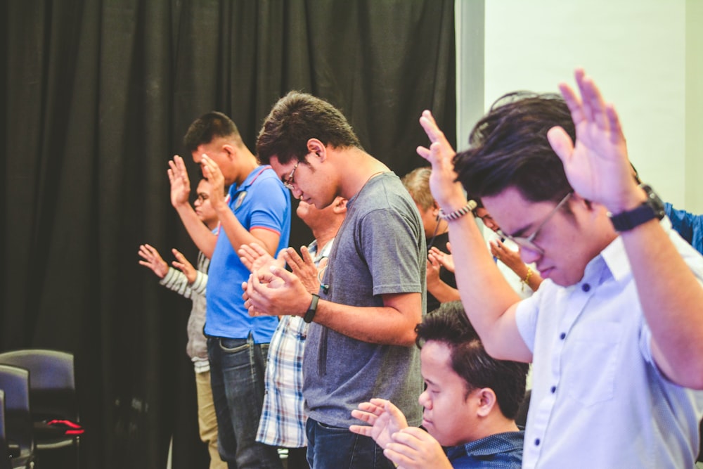 people raising hands while closing their eyes inside room