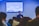 A person is speaking in front of an audience in a room with a screen displaying a biblical passage from Hebrews 11:32-40. The room appears to have subdued lighting with an emphasis on the speaker who is holding a microphone.