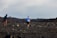 A person jogs across a rocky, barren landscape with another person in pursuit holding a camera stabilizer. The terrain is rough and covered with large stones, under an open sky. The individuals are dressed for outdoor activity and appear to be engaged in capturing footage.