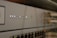 A close-up view of a network switch featuring a row of numbered indicator lights with some illuminated in white and green. The device has multiple Ethernet ports, and connectors are visible in the blurred background.