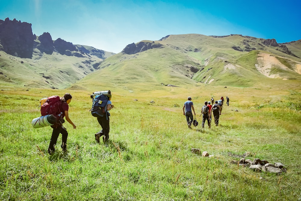 personnes marchant sur un champ vert près des montagnes