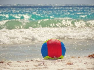 A vibrant beach ball bouncing on the sand near the ocean shore.