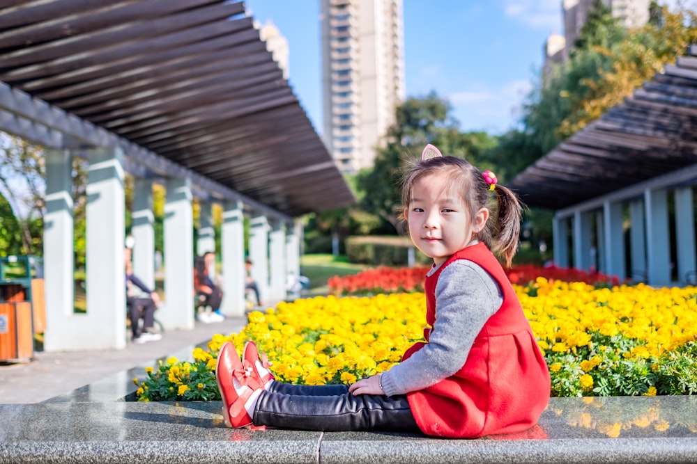 a little girl sitting on the ground in front of flowers