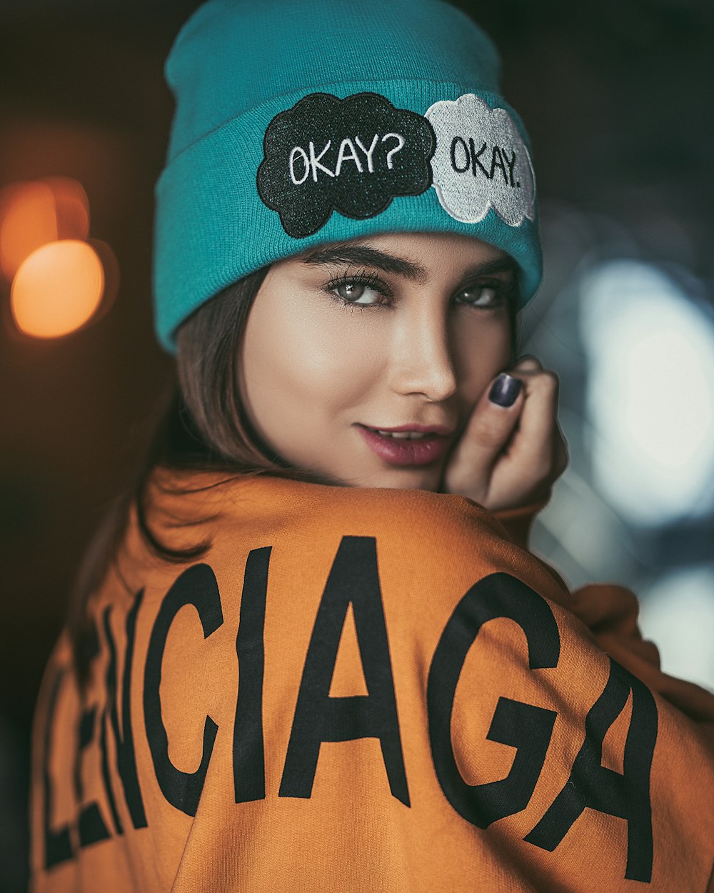 woman wearing orange and black sweater and teal beanie smiling