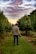 man walking on farm road under nimbus clouds