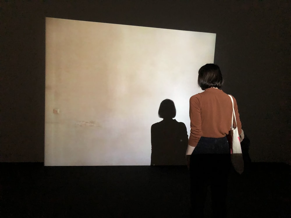 woman facing beige concrete wall with her shadow projected by the light