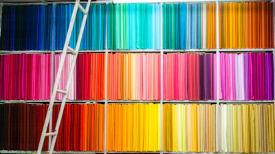 Rolls of smooth cotton fabric in various pastel shades stacked on wooden shelves