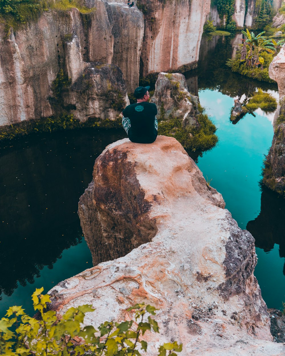 man sitting on cliff facing body of water