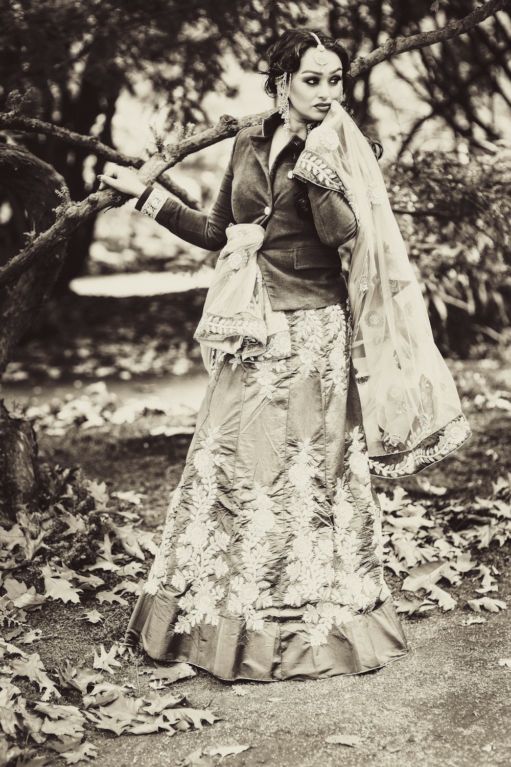 grayscale photography of woman standing beside tree