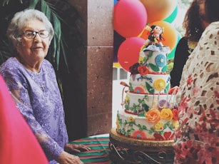 woman wearing purple floral long-sleeved dress besides 4-layer cake
