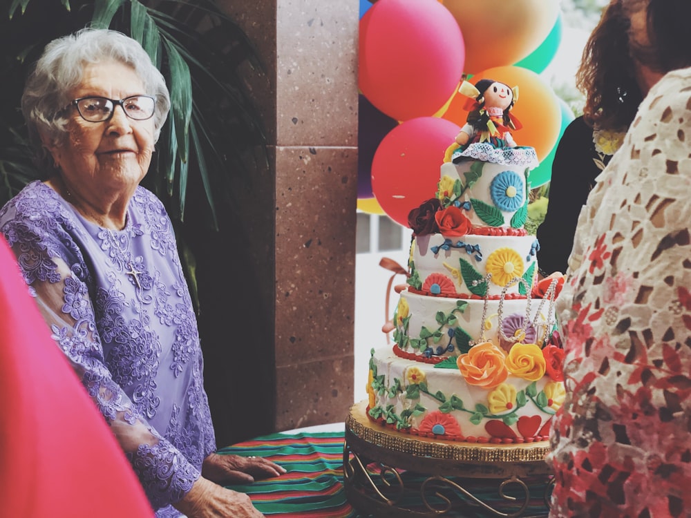 mulher usando vestido floral roxo de mangas compridas além de bolo de 4 camadas