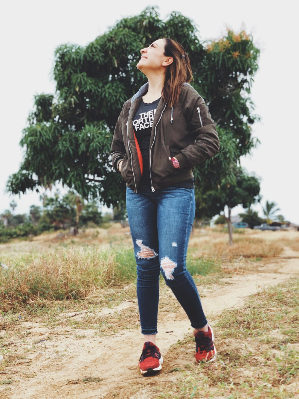 woman in brown jacket walking near green tree