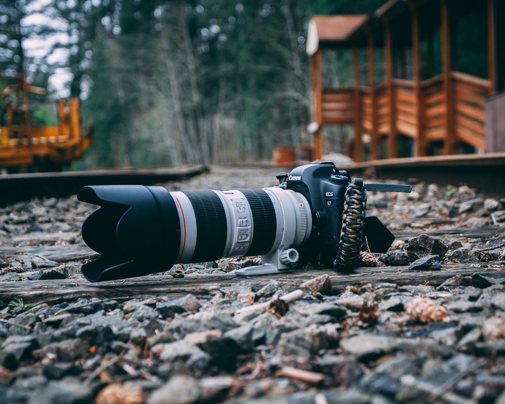appareil photo reflex numérique blanc et noir sur un sol rempli de pierres près d’un établissement en bois