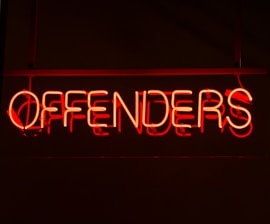 A neon sign displaying the word 'OFFENDERS' in vibrant red against a dark background.