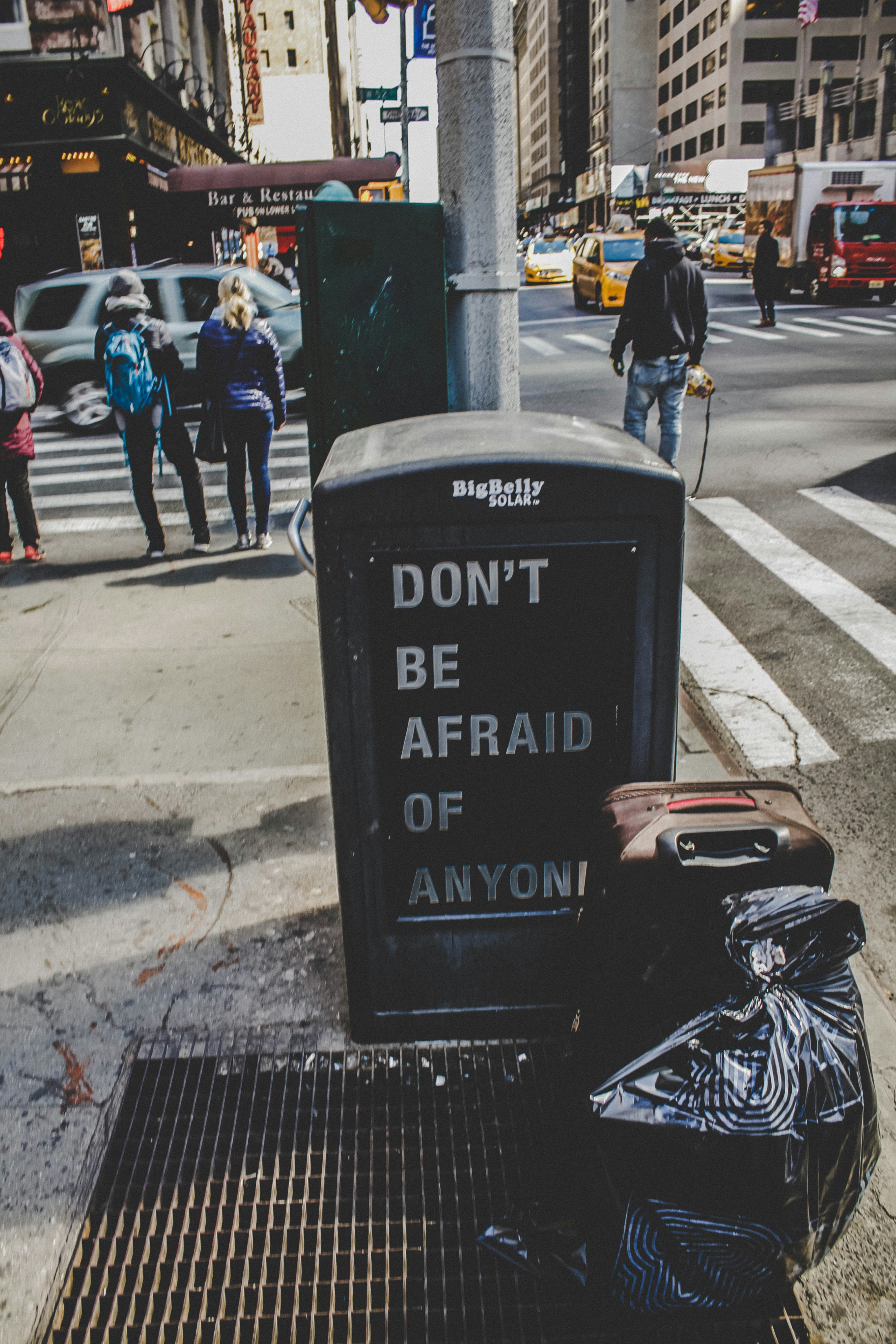 brown leather luggage beside street and sign of Don't be afraid of anyone