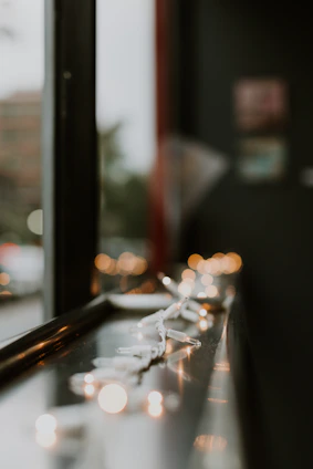 Battery-operated string lights twinkling softly around a window frame at dusk.