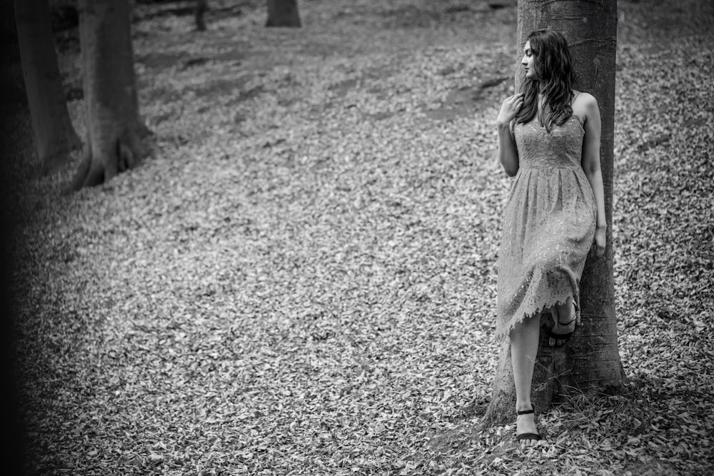 木にもたれかかってドレスを着た女性のグレースケール写真