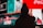 A silhouette of a person wearing a beanie is seen against a backdrop of brightly lit, colorful billboards with various advertisements, including recognizable brand logos.