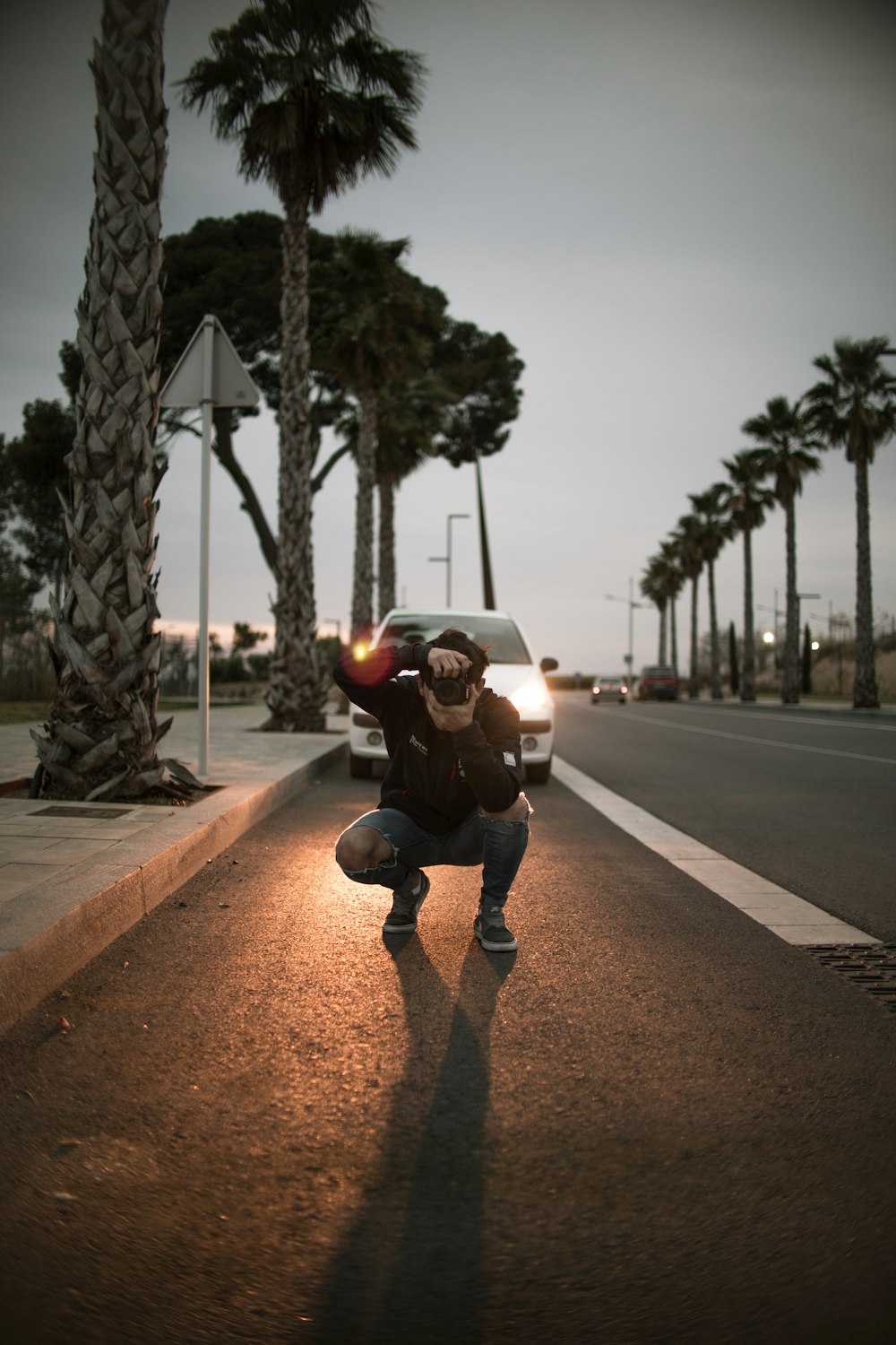 man using camera in front of white vehicle